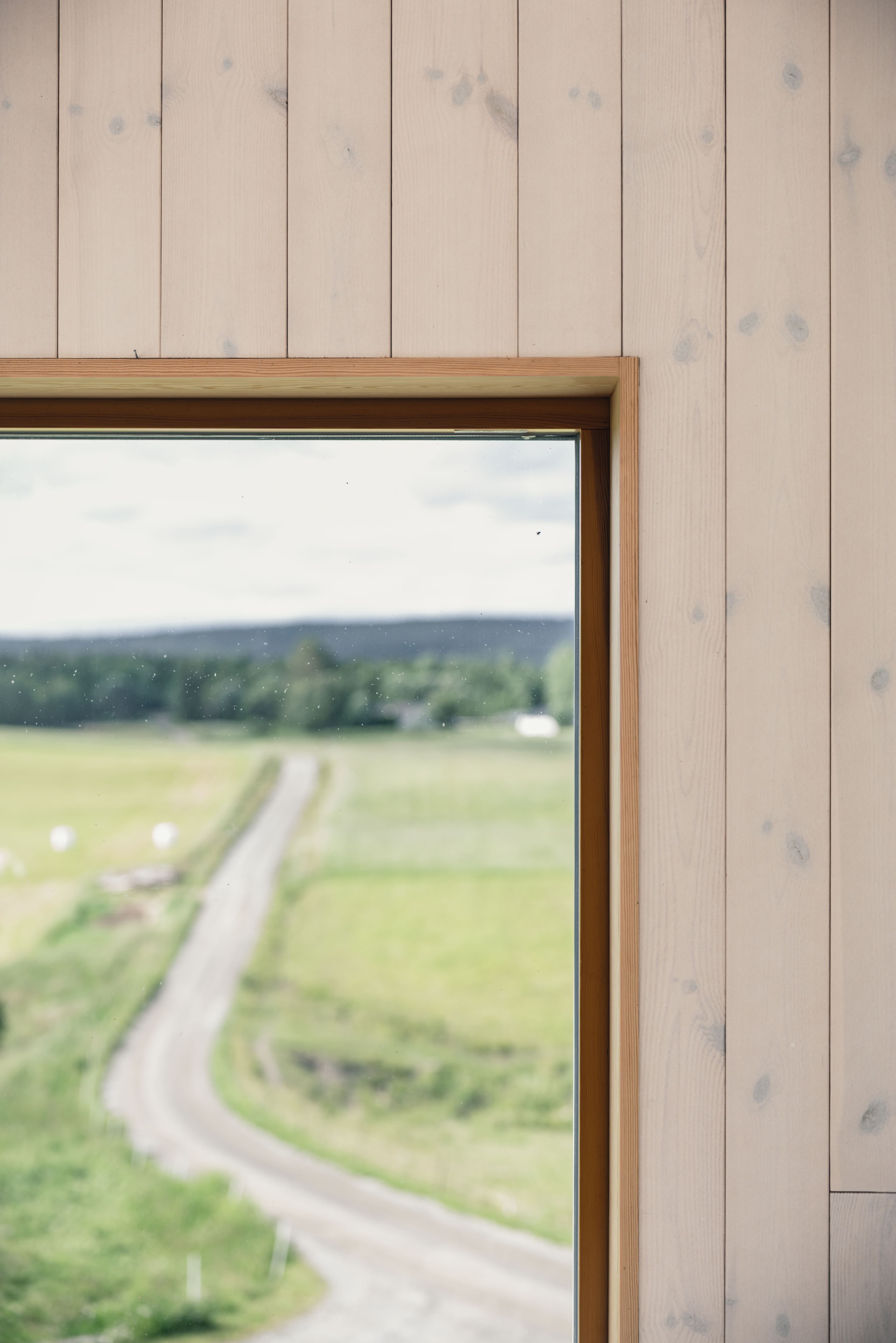 Invändig träpanel med ett fönster som vetter mot ett stillsamt lantligt landskap, kompletterad med väggpanel från Norrlands Trä i Putsad slätspont, superlasyr vit.